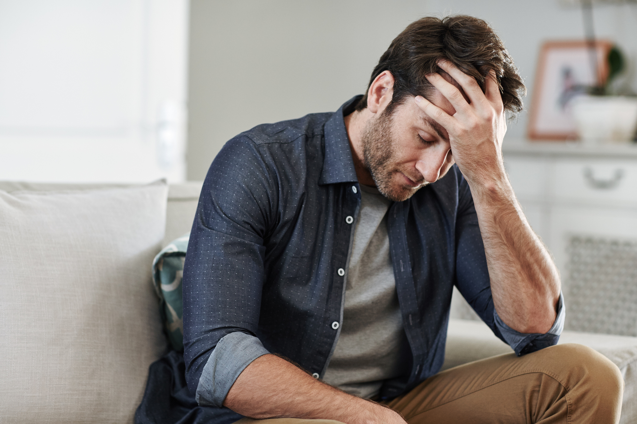 Man sitting on couch covering forehand with hand stressing and considering stress drinking