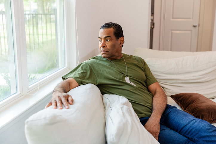 Depressed senior adult veteran looks out window of home Older male veteran looking out his window