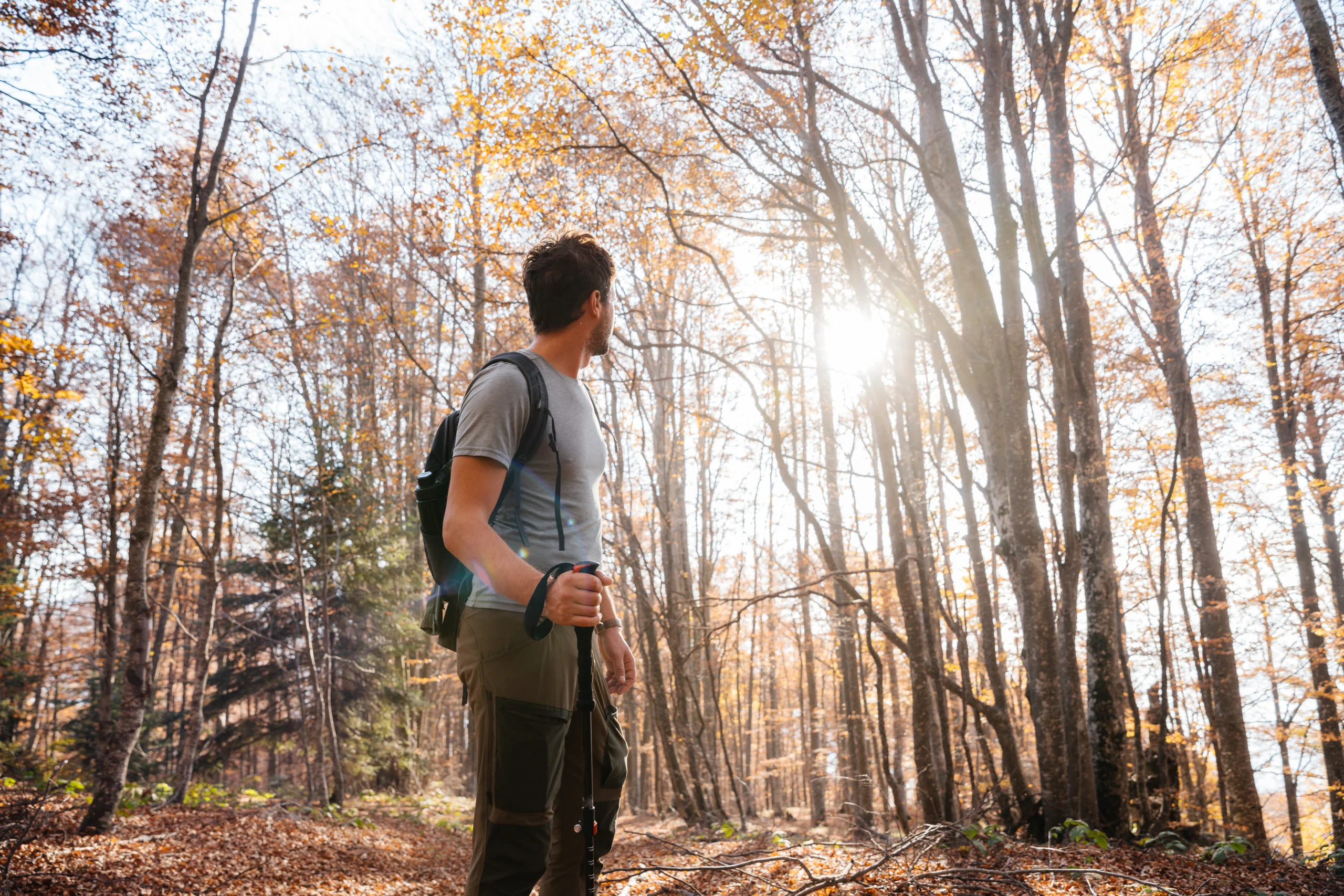 A man is hiking through a autumn landscape. He carries a sturdy backpack on his shoulder, suggesting he is well-prepared for the trek. The trail winds gently through the mountains, with glimpses of rolling hills and valleys in the background. Dressed in comfortable outdoor gear, the man appears immersed in the beauty of nature, enjoying the tranquility and solitude of the season.
