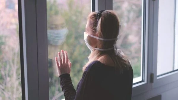 Woman with mask staring out window dealing with isolation during covid pandemic