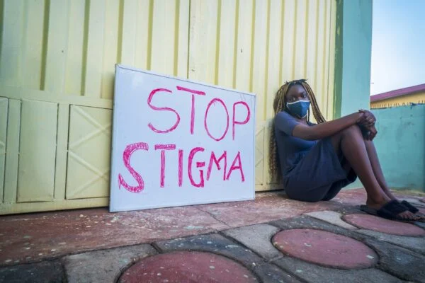 Young woman sitting next to sign that reads stop stigma