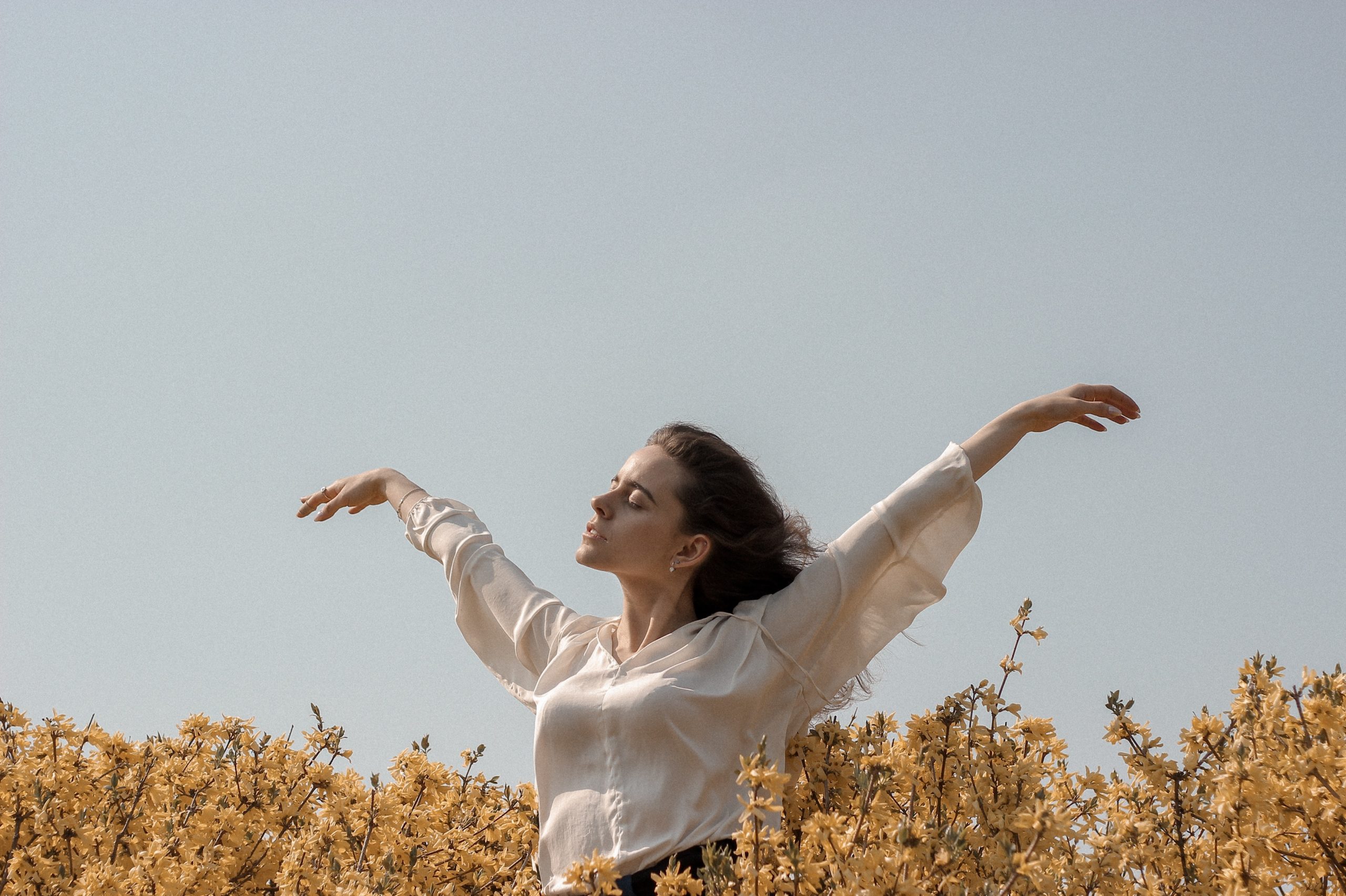 Woman in a field embracing the sun on her face with her arms spread wide