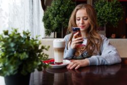 Young adult female sitting at a table looking at her phone with a coffee drink