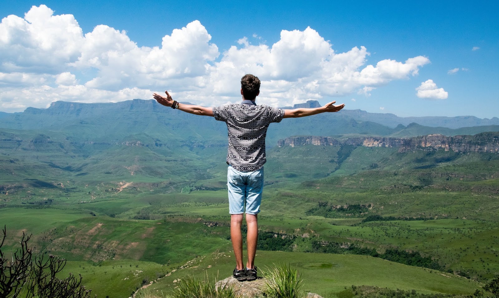 Man standing on a rock looking out over the valley with his arms spread wide