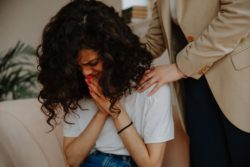 Upset woman with her hands pressed to her lips being consoled by a friend/family member