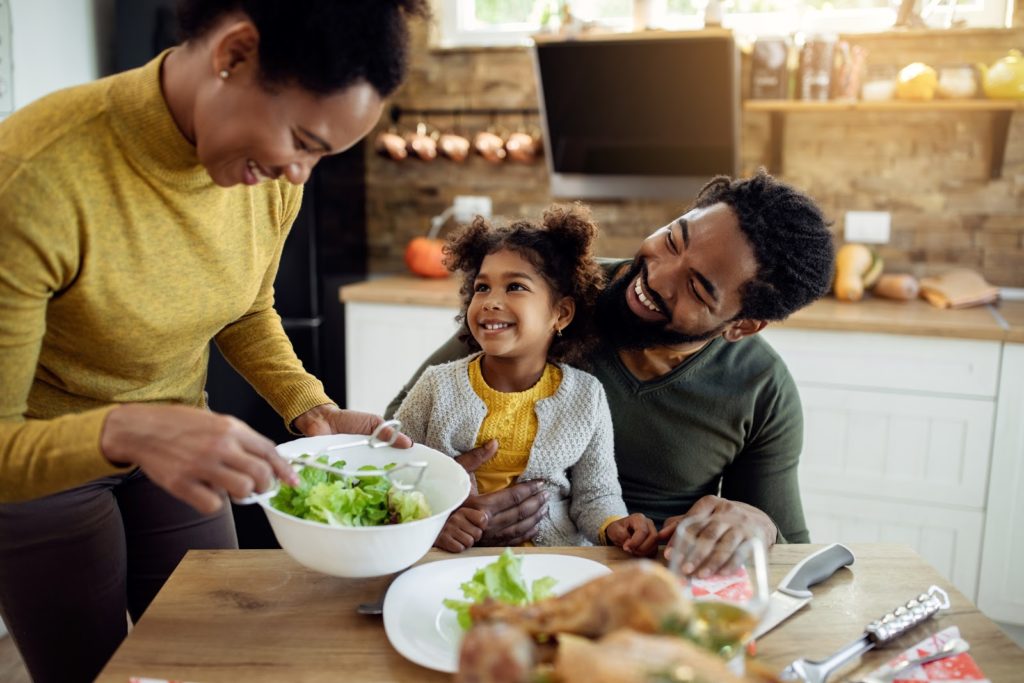 Happy black family celebrating Thanksgiving and having lunch together in dining room. Focus is on girl.