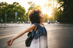 Young adult woman relaxing on the street at sunset in the city in summer opening your arms and looking upwards with closed eyes and smiling - Millennial is free and carefree