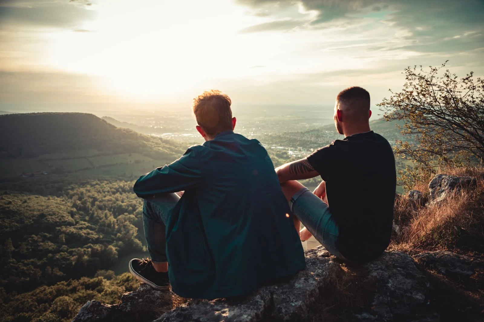 Two men sitting on top of a mountain looking out over the valley below