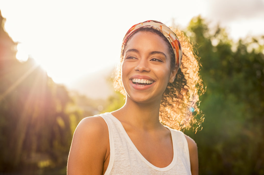 Portrait of beautiful african american woman smiling and looking away at park during sunset. Outdoor portrait of a smiling black girl. Happy cheerful girl laughing at park with colored hair band.