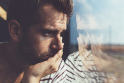 Sad young man looking through the window