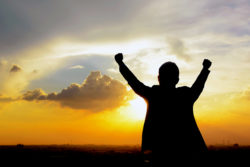 Silhouette of a man raising his arms in twilight sky background - success, winning & accomplished concepts