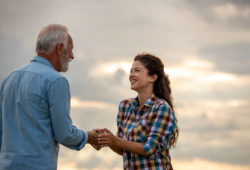 Young happy woman holding hand of senior man with both palms, shaking hands. Clouds in background