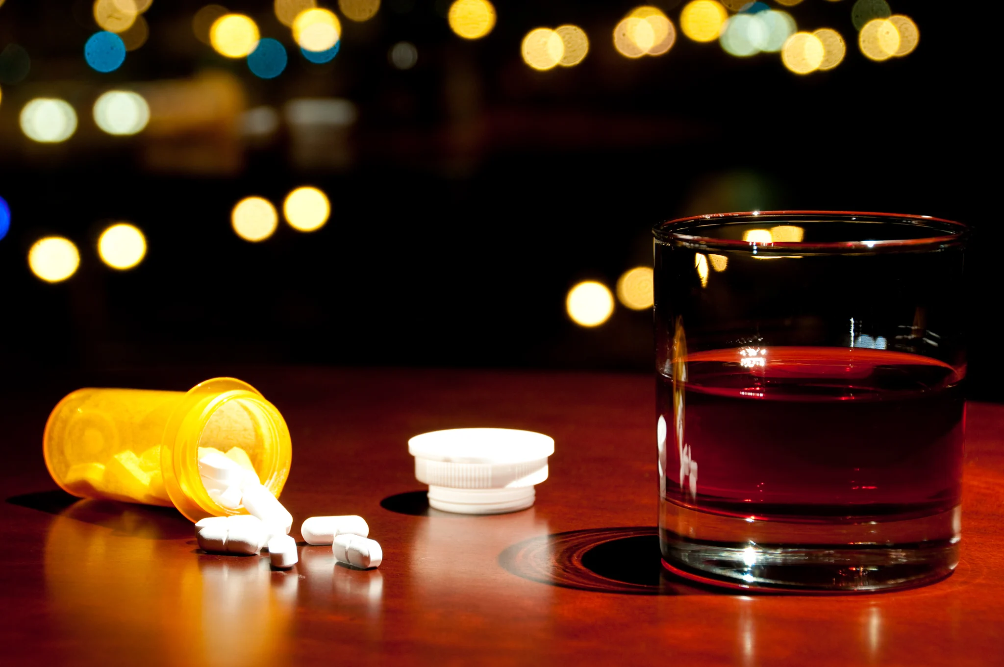 pills spilled out of a bottle on a table next to a glass of alcohol