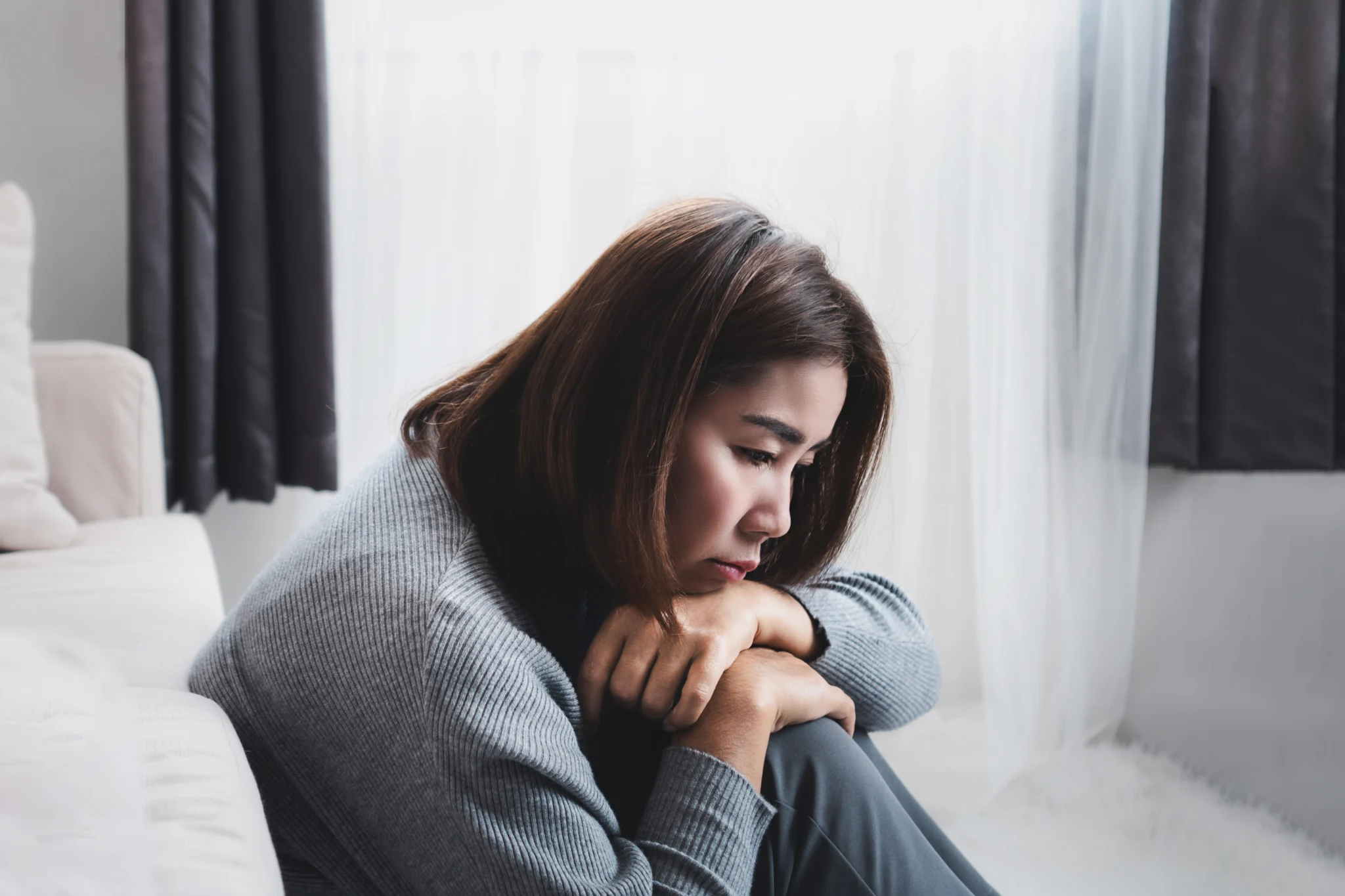sad Asian woman sitting alone in a room due to depressive disorder, mental health issues, anhedonia concept