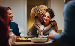 Cheerful smiling African-American woman embracing her female friend during a dinner with family and friends.