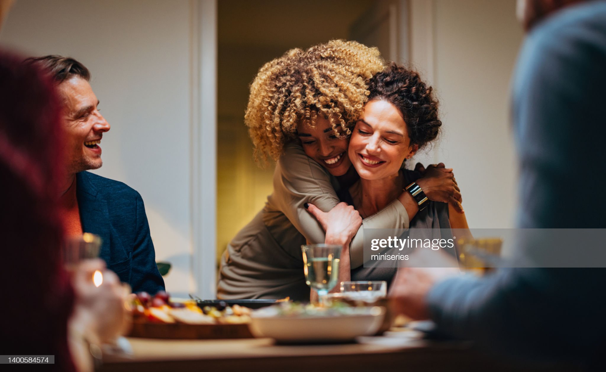 Cheerful smiling African-American woman embracing her female friend during a dinner with family and friends.