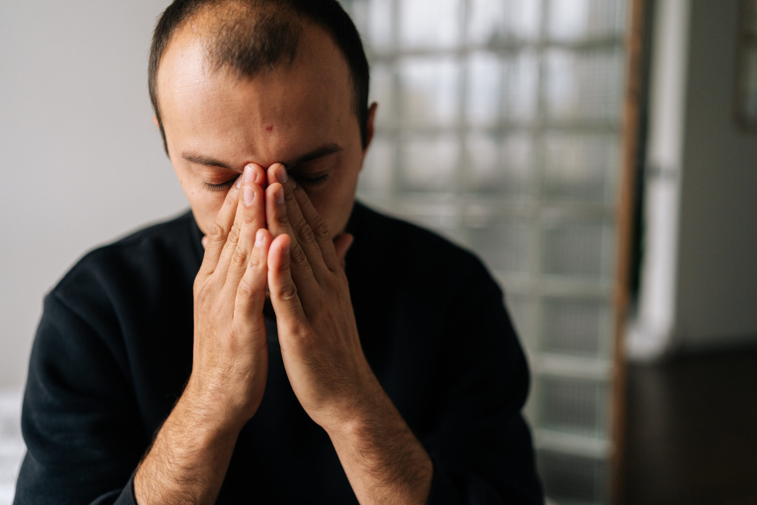 Close-up face of depressed male sitting alone at home holding face with hand, deep thoughts feeling lonely. Frustrated young man pondering make difficult choice, suffers from mental pain, heartbreak.