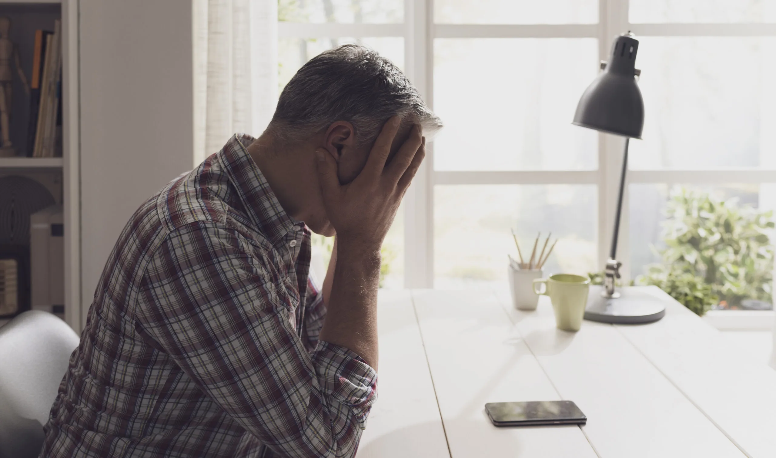 Desperate man waiting for a phone call at home, he is staring at the phone with head in hands