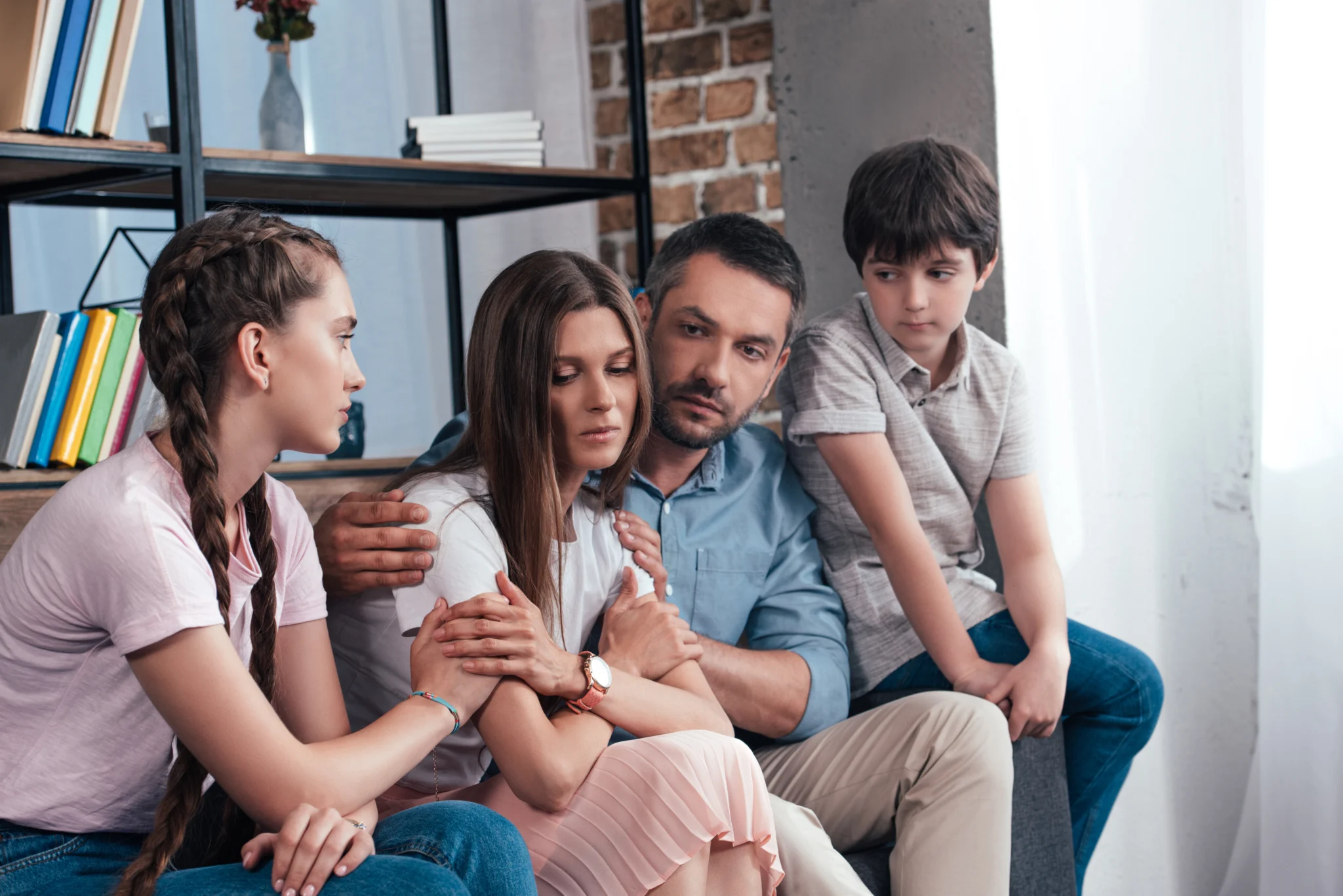 family embracing and cheering up frustrated woman on sofa in counselor office