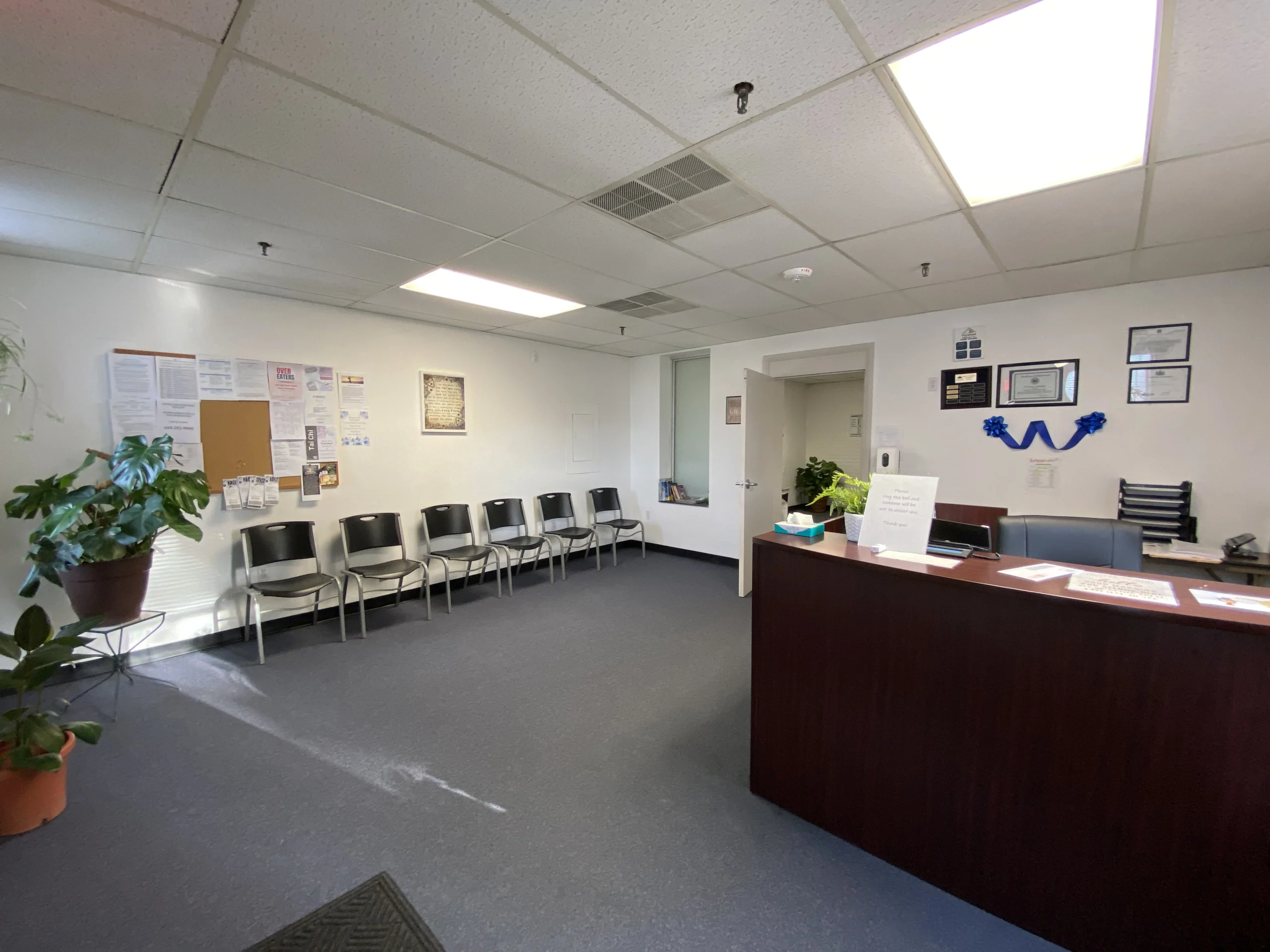 White room with row of black chairs along the left wall and reception desk on the right side