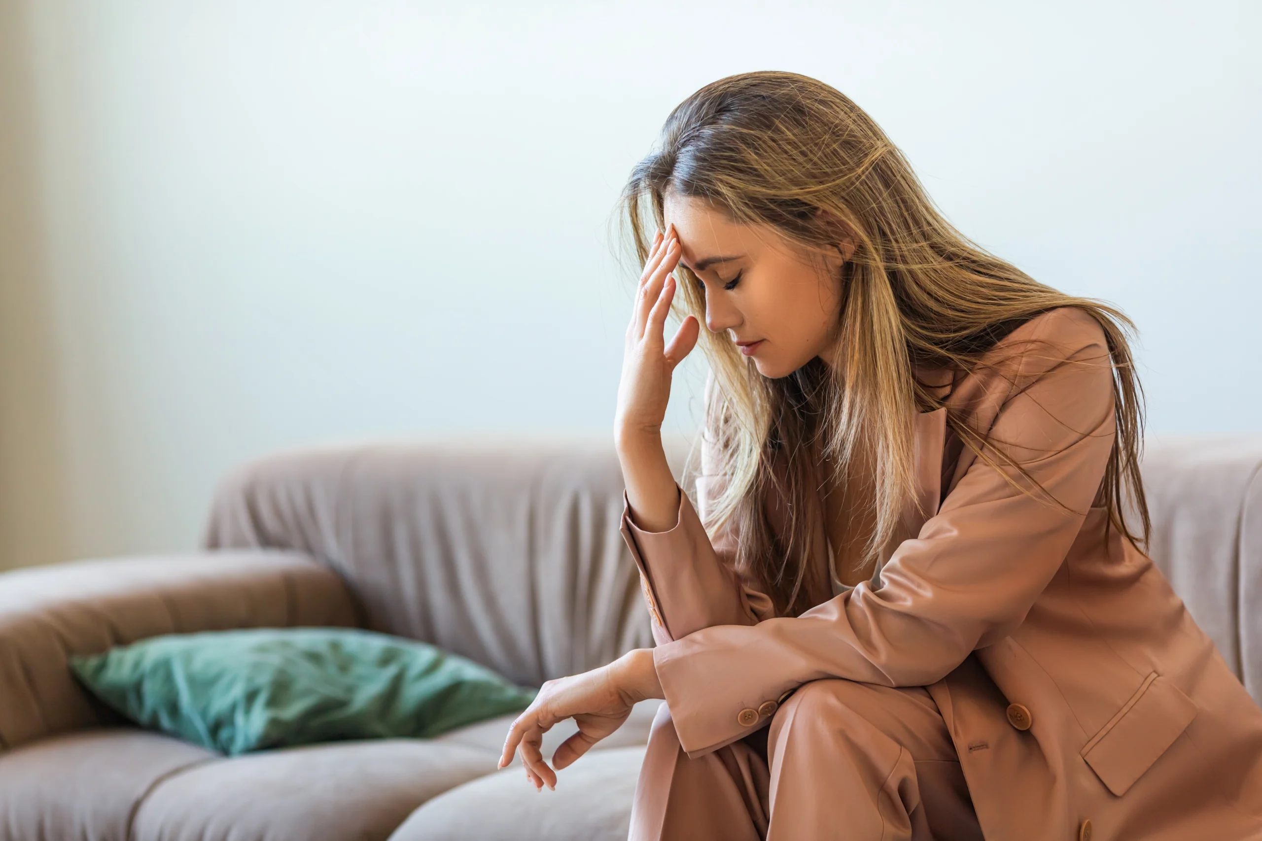 Mentally burnt out and completely devastated, the young woman sits on the couch with her head in her hands. The businesswoman has lost her motivation to work and live. Close-up photo.