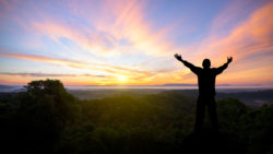 Silhouette of man raised hands with landscape mountains at sunset