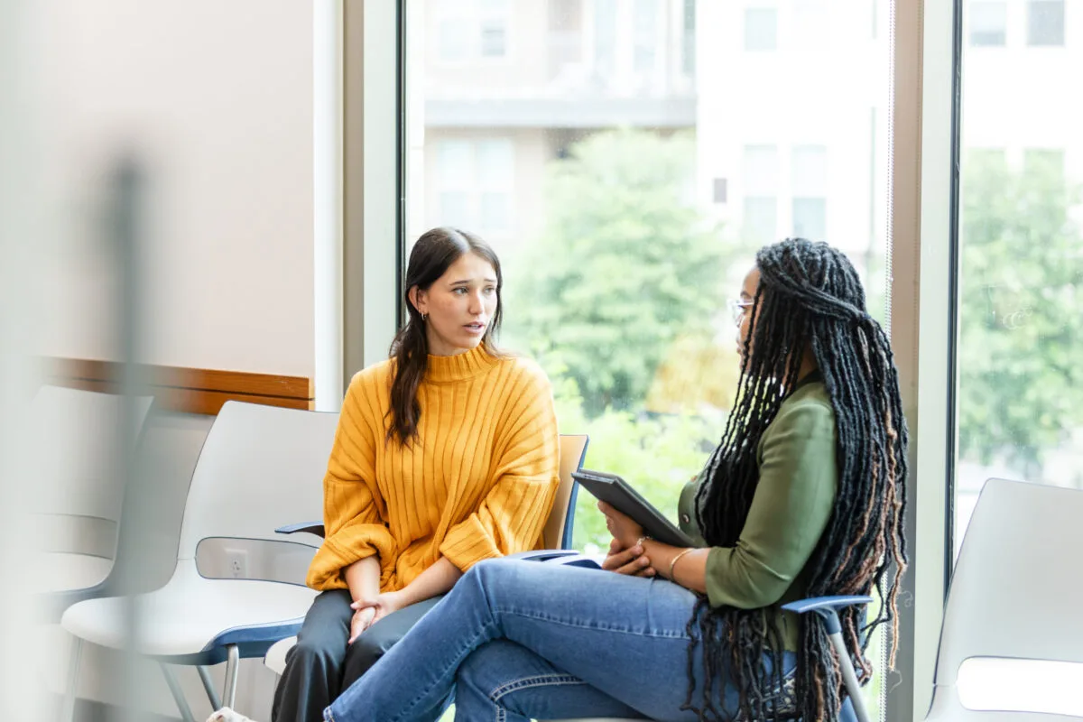 The young adult woman looks worried as she listens to the unrecognizable young adult female therapist.